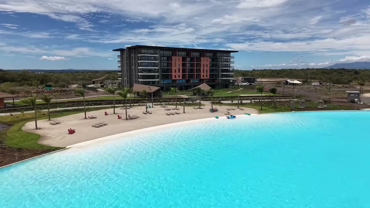 Aerial view of synthetic thatch palapas beside a residential tower and a lagoon, Guanacaste